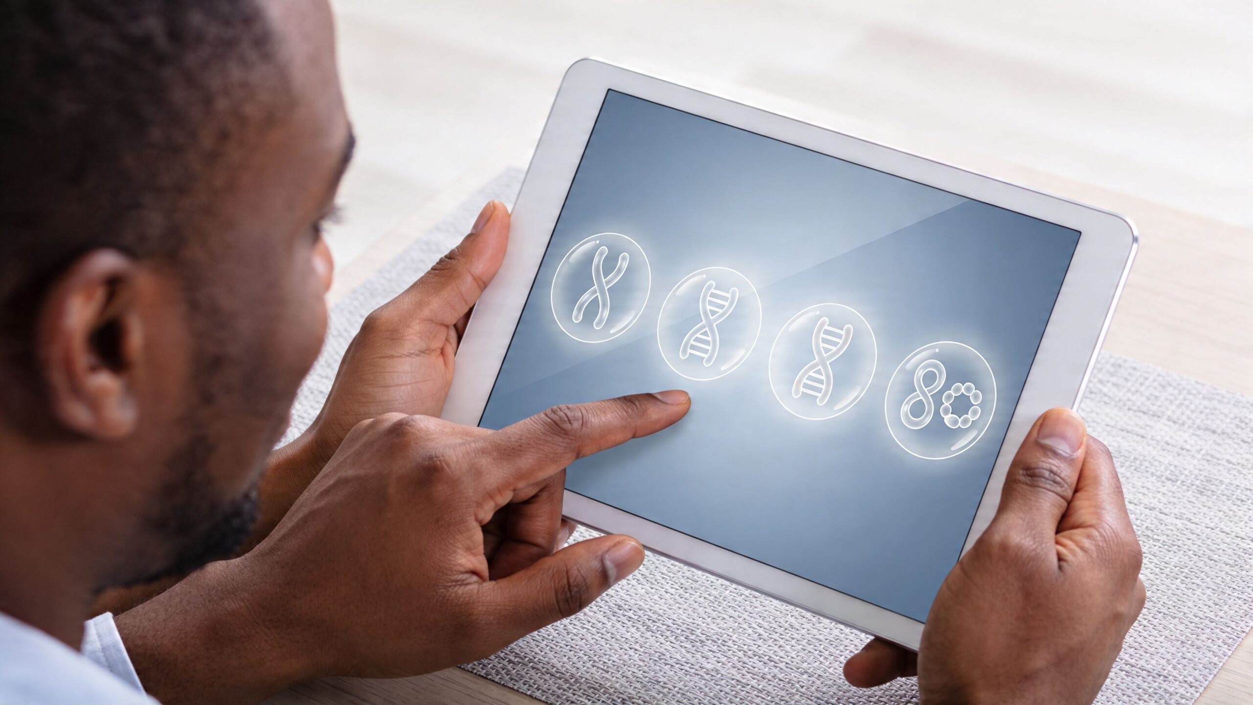 A person using a tablet to navigate a screen displaying various DNA and genetic chromosome icons.