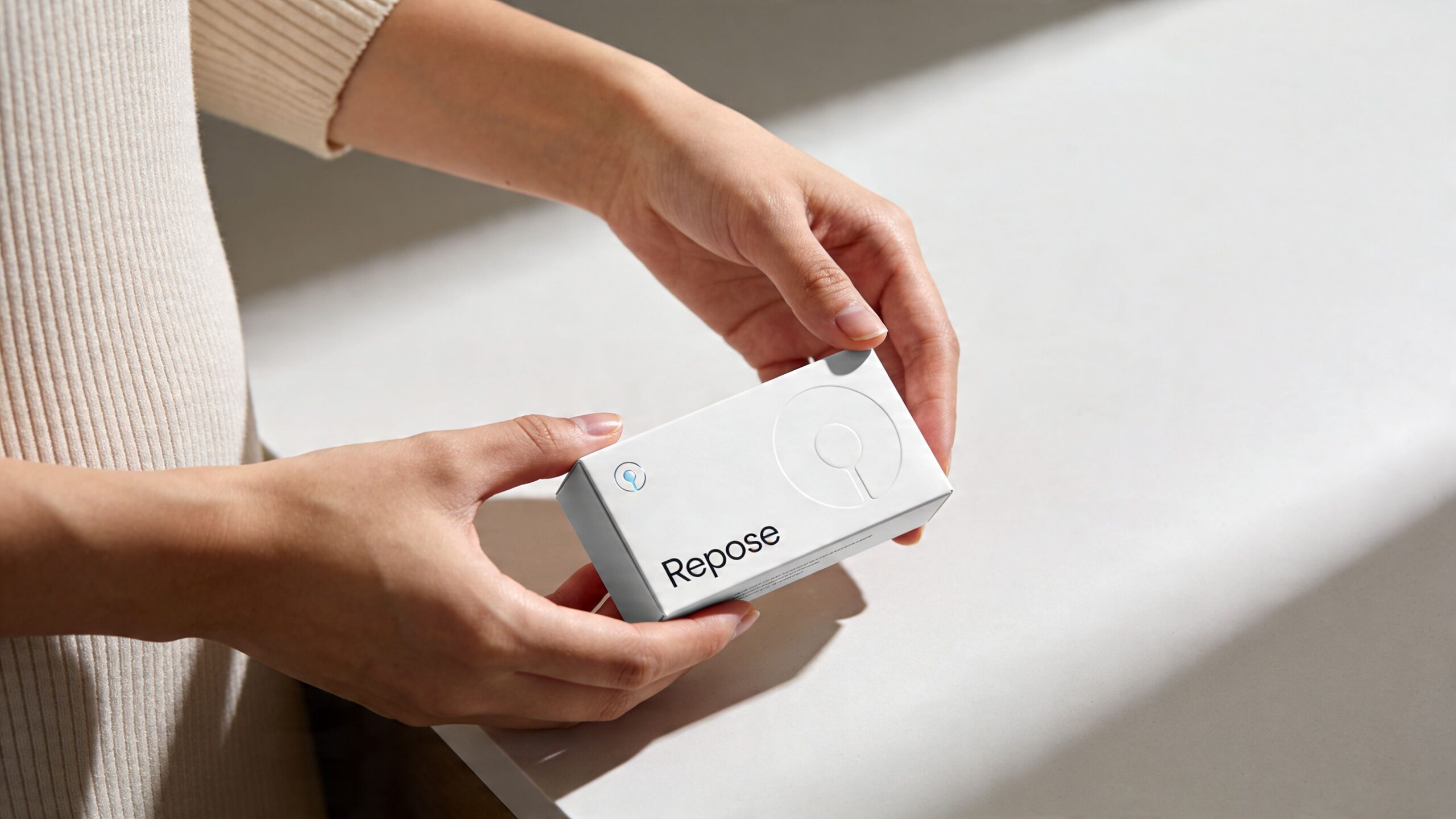 A person holding a small white box labeled Repose, showcasing the product packaging design in a minimalist setting.